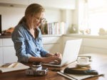 Young woman sitting in her kitchen working on a laptop