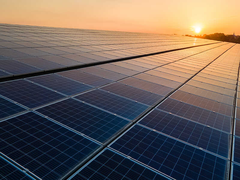 Blue photovoltaic solar panels mounted on building roof for producing clean ecological electricity at sunset. Production of renewable energy concept.