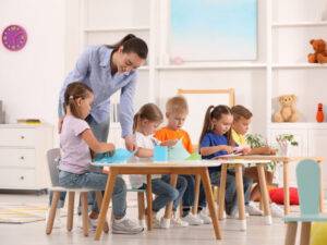 Nursery,Teacher,With,Group,Of,Cute,Little,Children,Drawing,And