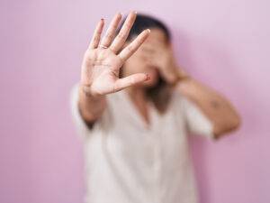 Blonde woman standing over pink background covering eyes with hands and doing stop gesture with sad and fear expression. embarrassed and negative concept.